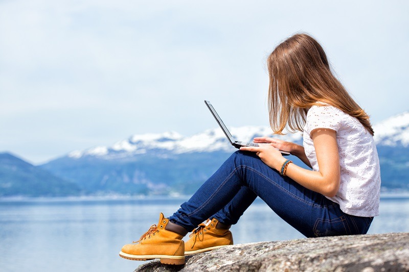 girl hiker with a laptop sitting on a rock on a background of mountains and lakes